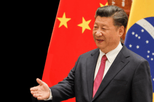 Chinese flag and Brazilian flag visible behind a man in business attire speaking at a formal event