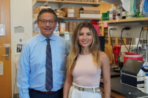 Two UCLA researchers pose in a laboratory setting with shelving and equipment visible in the background.
