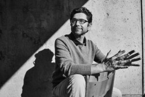 Artem Patapoutian, Nobel Laureate and MCDB Alumnus, sits with his hand extended against a wall with dramatic lighting.
