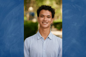 Portrait of a student in a light blue shirt against a blurred outdoor background.