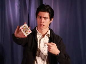 Nathaniel Grandinetti, an MCDB major, performs a magic trick with playing cards while wearing a blazer and dress shirt.