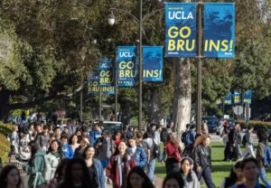 Crowd of students and visitors on UCLA campus with blue "Go Bruins" banners hanging from trees.