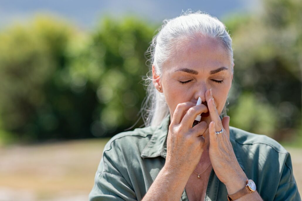 Person demonstrating nasal spray technique by closing one nostril while applying spray to the other nostril.
