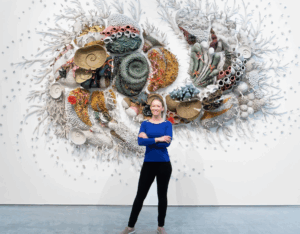 Artist Courtney Mattison standing in front of her sculpture of a coral reef.